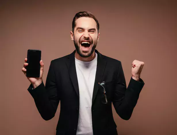 man-rejoices-and-poses-with-smartphone-on-brown-background